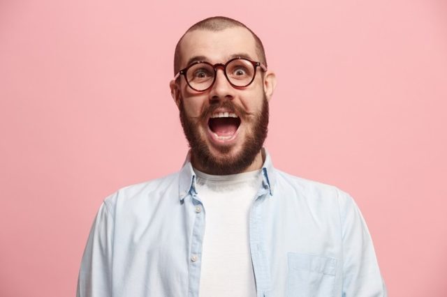 Surprised-looking bearded man wearing blue shirt against pink background